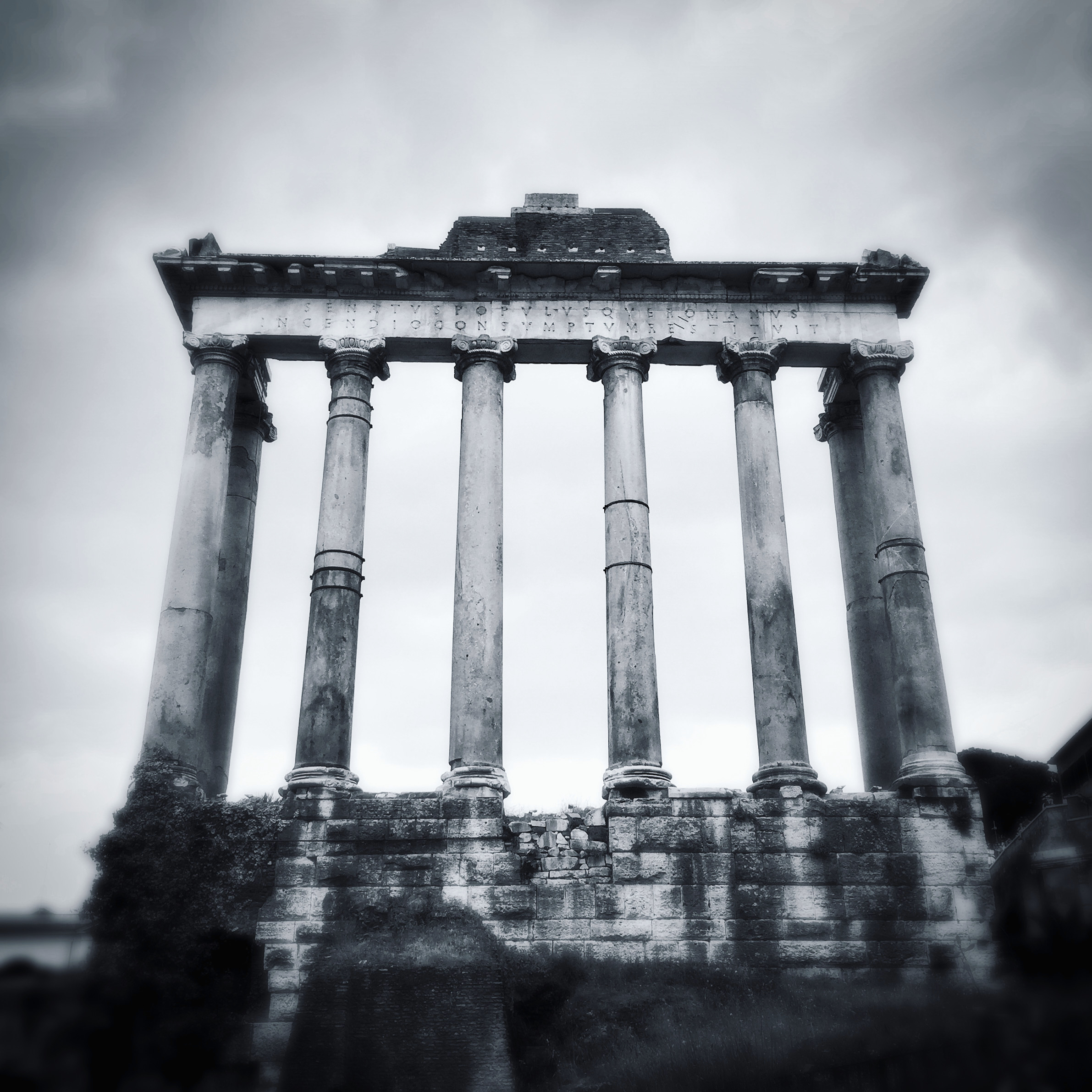 A black and white photo of a set of columns in the Imperial Forum in Rome, Italy.